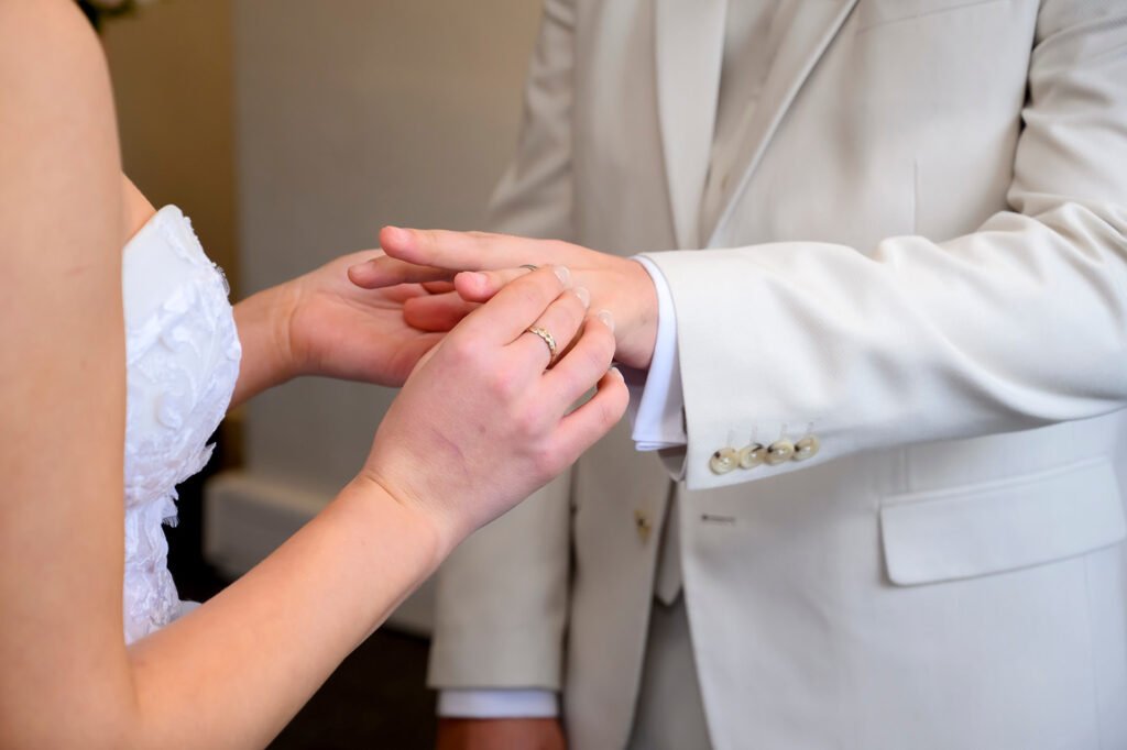 Close up of groom placing wedding ring on bride's finger.